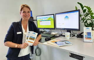 Eine Frau steht am Schreibtisch und hält Flyer in den Händen.