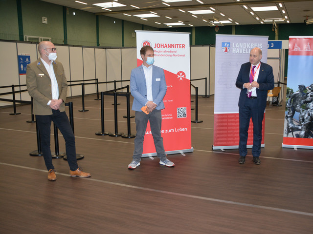 Drei Männer stehen in einigem Abstand nebeneinander in der Havellandhalle, die zum Impfzentrum umgebaut wurde.