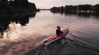 Ein Mann sitzt in einem Kanu und blickt über das Wasser Richtung Sonnenaufgang