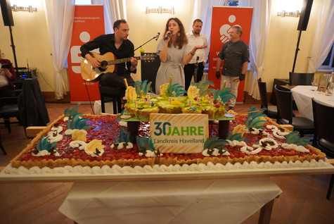 Die 30-Jahre-Havelland-Torte steht im Saal, dahinter macht ein Duo Musik - Klick öffnet Bildbetrachter