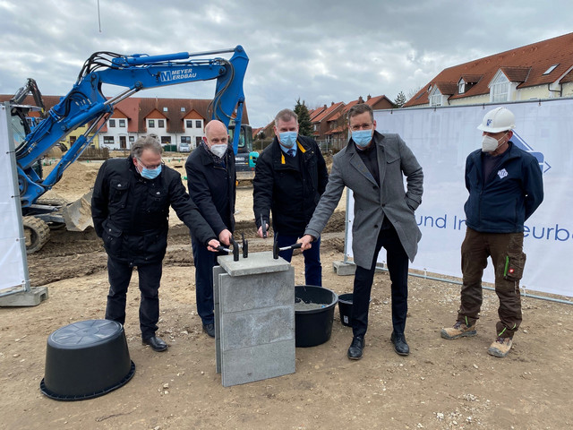 Vier Männer mit einem Hammer in der Hand stehen verteilt um den Grundstein herum.