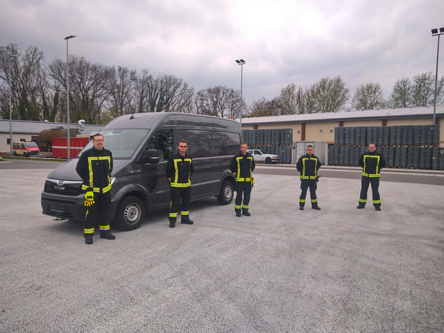 Fünf Männer in Feuerwehrkleidung stehen vor einem Trasporter.