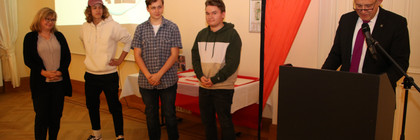 Der Landrat steht am Rednerpult und hält eine Laudatio. Daneben stehen die Preisträger.