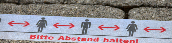 Eine Klebestreifen auf dem Boden mit der Aufschrift: Bitte Abstand halten!