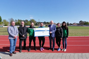 7 Personen stehen auf der Laufbahn im Premnitzer Stadion und die 3 in der Mitte halten den symbolischen Spendenscheck. - Klick öffnet Bildbetrachter