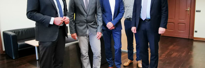 Fünf Männer stehen in einem Büro nebeneinander und schauen in die Kamera.