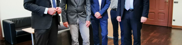 Fünf Männer stehen in einem Büro nebeneinander und schauen in die Kamera.