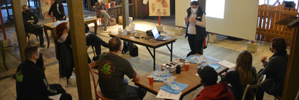 Eine Gruppe von Menschen sitzt in einem Raum. Eine Person steht vor der Gruppe und erklärt etwas.