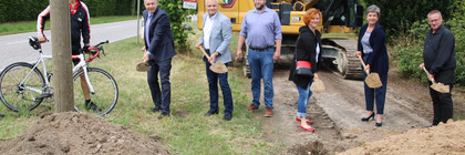 Mehrere Menschen stehen in einer Reihe und führen einen Spatenstich aus.