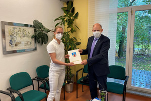 Denise Meseck und Landrat Lewandowski schauen in die Kamera. Zwischen sich halten sie den Zuwendungsbescheid.