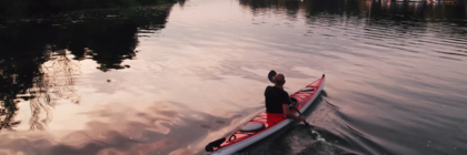 Ein Mann sitzt in einem Kanu und blickt über das Wasser Richtung Sonnenaufgang