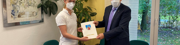 Denise Meseck und Landrat Lewandowski schauen in die Kamera. Zwischen sich halten sie den Zuwendungsbescheid.