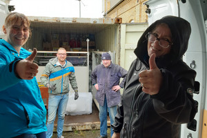 Mitglieder des Vereins Hand in Hand stehen am Container mit den eingeladenen Tafeln und schauen in die Kamera.