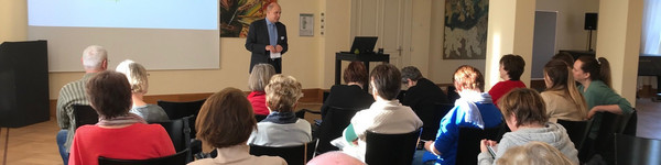 Klick öffnet Bildbetrachter, Mann spricht vor Gruppe von Menschen