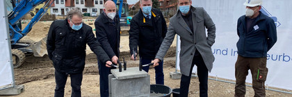 Vier Männer mit einem Hammer in der Hand stehen verteilt um den Grundstein herum.
