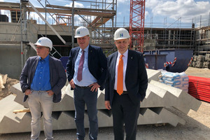 Drei Männer mit Bauhelm stehen auf einer Baustelle.