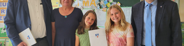 Fünf Personen stehen in einem Klassenraum, im Hintergrund die Tafel und Projektplakate an der Wand - Klick öffnet Bildbetrachter