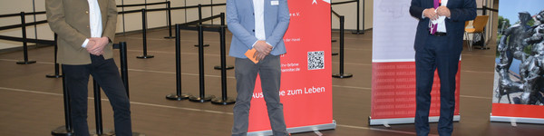 Drei Männer stehen in einigem Abstand nebeneinander in der Havellandhalle, die zum Impfzentrum umgebaut wurde.