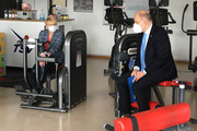 Landrat Lewandowski und Birgit Faber sitzen auf Sportgeräten in einem Fitness-Raum und unterhalten sich..