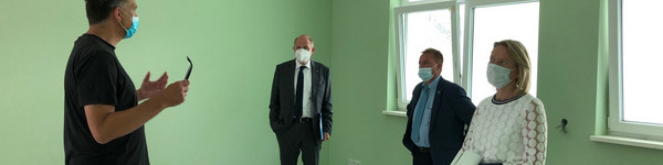 Vier Personen stehen in einem grün gestrichenen Raum und reden miteinander.