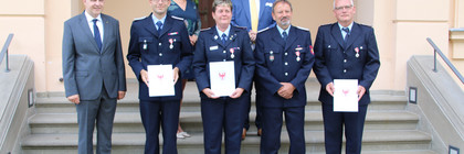 Die ausgezeichneten Feuerwehrleute stehen mit dem Landrat und zwei weiteren Personen auf einer Treppe.