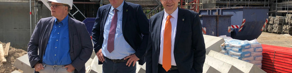 Drei Männer mit Bauhelm stehen auf einer Baustelle.