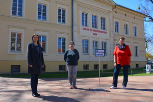 Drei Frauen stehen auf einem Platz, im Hintergrund ist das FGZ Nauen zu sehen.