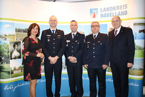 Drei Feuerwehrleute stehen zwischen der Kreistagsvorsitzenden und dem Landrat und lächeln in die Kamera.