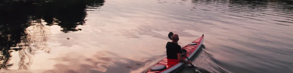 Ein Mann sitzt in einem Kanu und blickt über das Wasser Richtung Sonnenaufgang