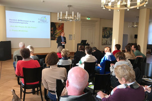 Klick öffnet Bildbetrachter, Mann spricht vor Gruppe von Menschen