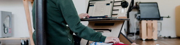 Eine Frau arbeitet am Computer und streichelt nebenbei ihr kleines Kind.