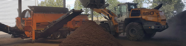 Ein Bagger schüttet Abfall in die Kompostieranlage, davor liegt ein großer Haufen Kompost - Klick öffnet Bildbetrachter