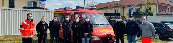 Einige Feuerwehrleute stehen auf einem Parkplatz vor einem Feuerwehrfahrzeug.