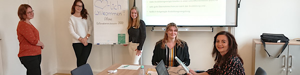 Fünf Frauen sitzen und stehen verteilt in einem Raum.