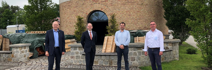 Vier Männer stehen vor einem Turm nebeneinander und schauen in die Kamera.