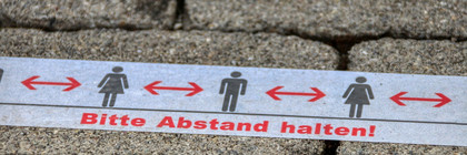 Eine Klebestreifen auf dem Boden mit der Aufschrift: Bitte Abstand halten!
