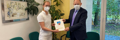 Denise Meseck und Landrat Lewandowski schauen in die Kamera. Zwischen sich halten sie den Zuwendungsbescheid.