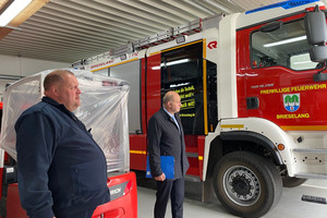 Zwei Männer stehen neben einem Feuerwehrauto.