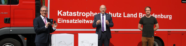 Harry Bräuer, Roger Lewandowski und Christoph Bajohr stehen vor einem Rettungsfahrzeug und zeigen zwei Schutzbrillen.