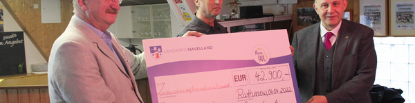 Drei Männer stehen in einem Raum und halten gemeinsam einen großen Scheck in den Händen.