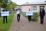Die beiden Schulleiter, der Bürgermeister und der Landrat stehen auf dem Außengelände der Oberschule in Premnitz. Die Schulleiter halten einen großen Scheck in den Händen, auf dem die jeweilige Fördersumme vermerkt ist.
