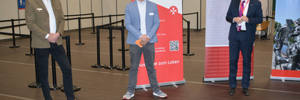 Drei Männer stehen in einigem Abstand nebeneinander in der Havellandhalle, die zum Impfzentrum umgebaut wurde.