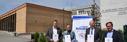 Vier Personen stehen vor einer Schule und halten jeweils eine Mappe in der Hand - Klick öffnet Bildbetrachter