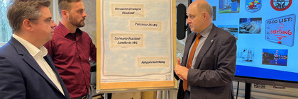 Drei Männer stehen vor einem Flipchart und unterhalten sich - Klick öffnet Bildbetrachter