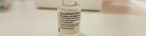 Eine Ampulle des Impfstoffes steht auf einem Tisch.