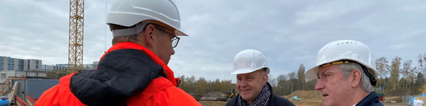 Drei Männer stehen auf einer Baustelle und unterhalten sich.