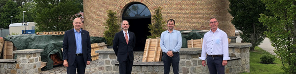 Vier Männer stehen vor einem Turm nebeneinander und schauen in die Kamera.