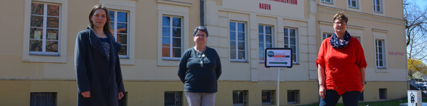 Drei Frauen stehen auf einem Platz, im Hintergrund ist das FGZ Nauen zu sehen.