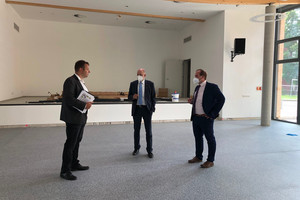 Drei Männer stehen im Halbkreis und unterhalten sich in der noch leeren neuen Halle.