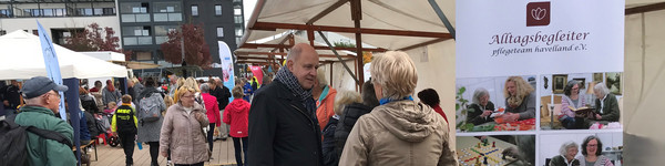 Klick öffnet Bildbetrachter, Mehrere Personen auf einem Platz an Ständen